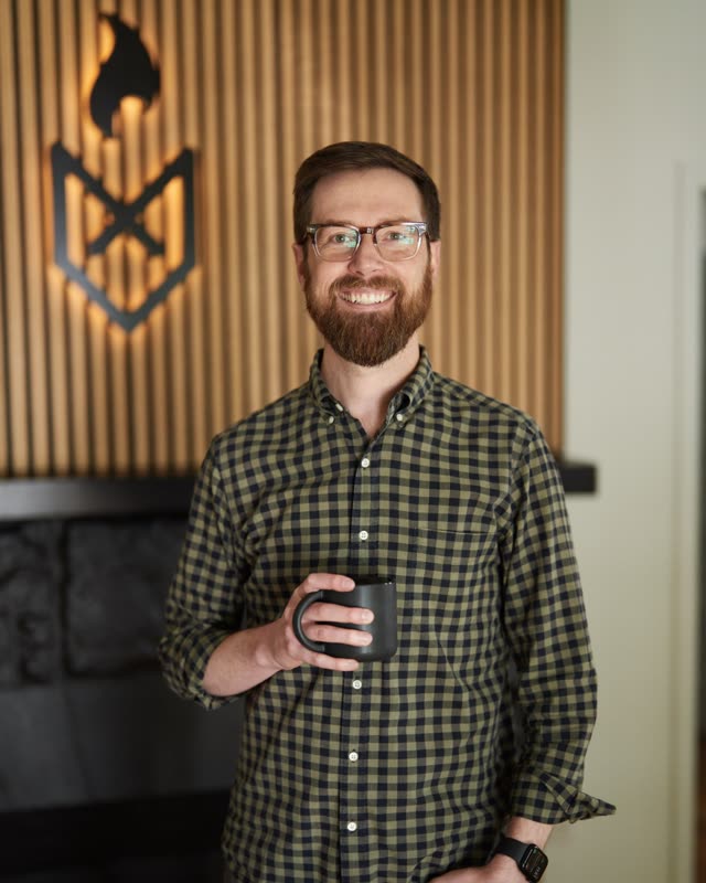 Colton Mulligan headshot: Standing with a coffee mug, FoxFuel logo behind him